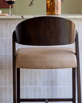 Enzo bar stool in dark wood with mocha leather seat, shown front view against white subway tile wall.