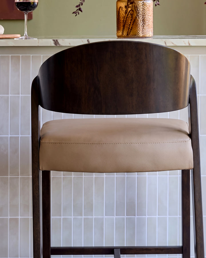 Enzo bar stool in dark wood with mocha leather seat, shown front view against white subway tile wall.