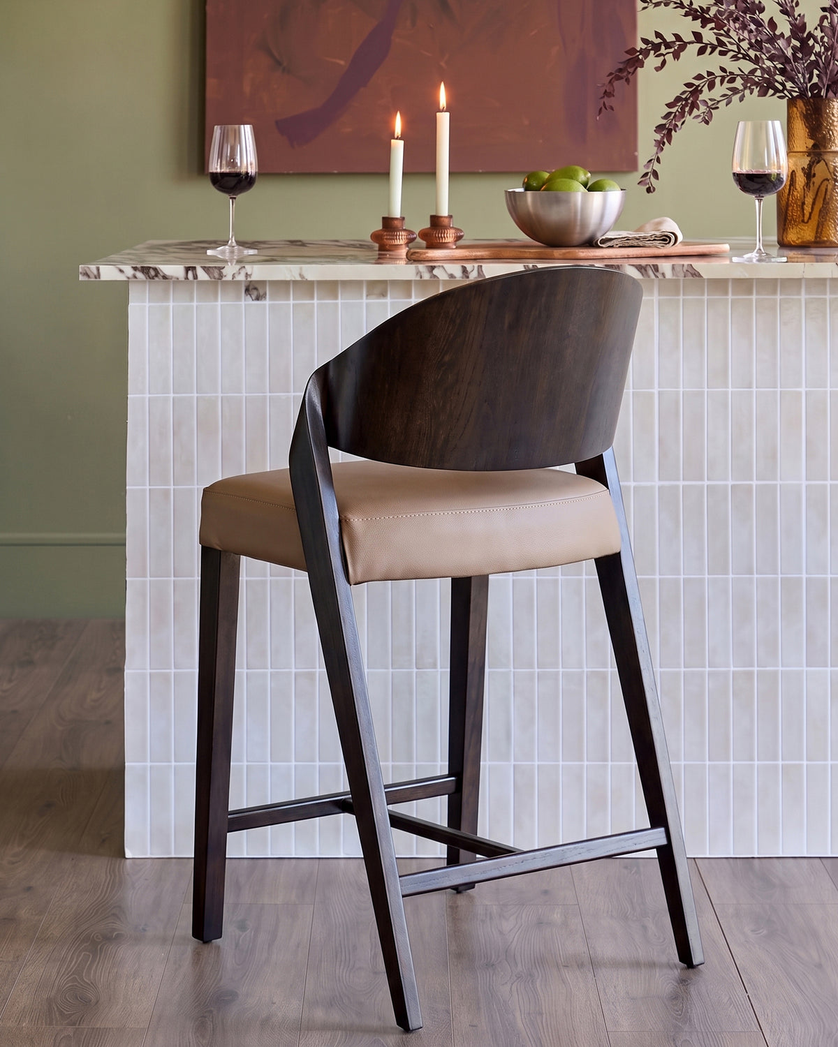 Enzo bar stool in mocha leather with dark wood frame, shown at white tile counter with wine glasses and candles.