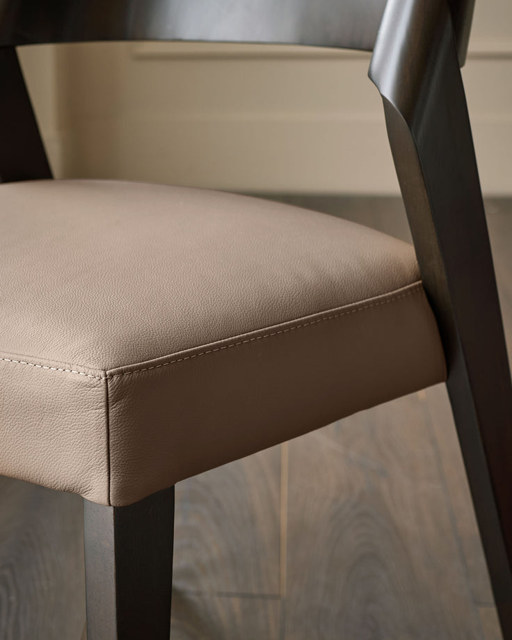Enzo dining chair in mocha leather, close-up detail showing stitched seat edge and metal frame leg.
