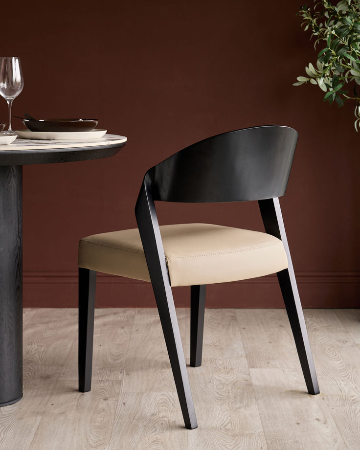 Enzo dining chair in black wood with natural leather seat, shown at round table with place setting against burgundy wall.