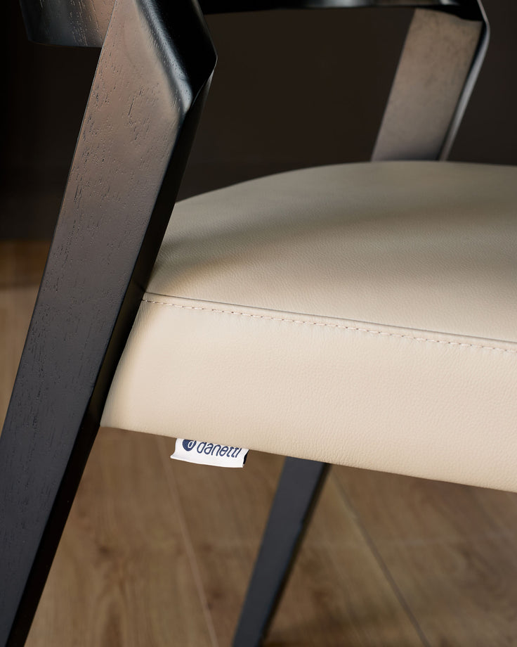 Enzo dining chair in natural leather, showing cream-colored seat with dark wood legs and backrest detail.