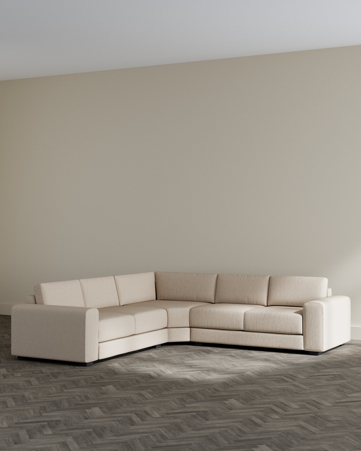 Modern beige L-shaped sectional sofa with a chaise on the left side, featuring clean lines and plush cushioning, presented in a room with light grey walls and dark herringbone wooden flooring.