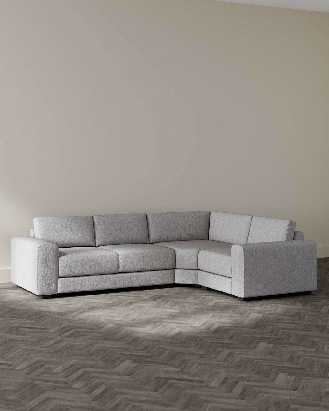 Contemporary light grey sectional sofa with a minimalist design, featuring clean lines, a low back, and wide armrests on a herringbone-patterned dark wood floor.