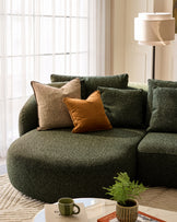 Dark green upholstered left-hand corner chaise sofa with curved design, styled with patterned and tan pillows in a bright living room setting.