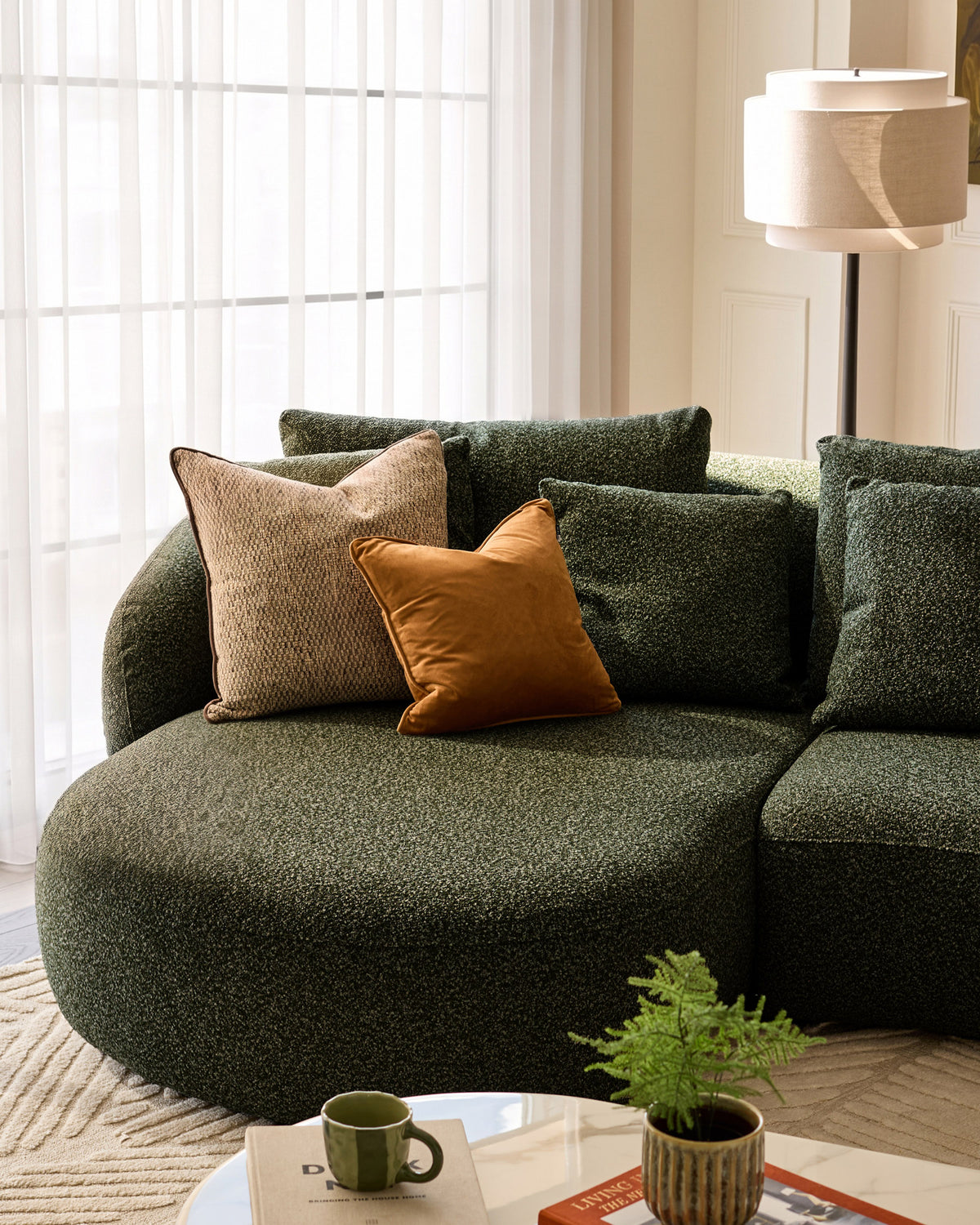 Dark green upholstered left-hand corner chaise sofa with curved design, styled with patterned and tan pillows in a bright living room setting.