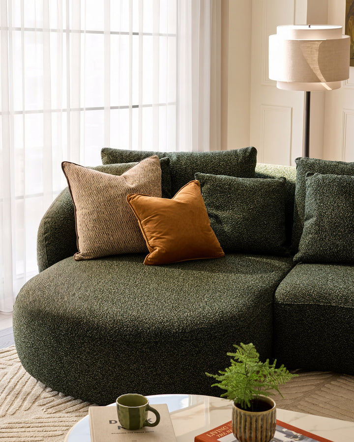 Dark green upholstered left-hand corner chaise sofa with curved design, styled with patterned and tan pillows in a bright living room setting.
