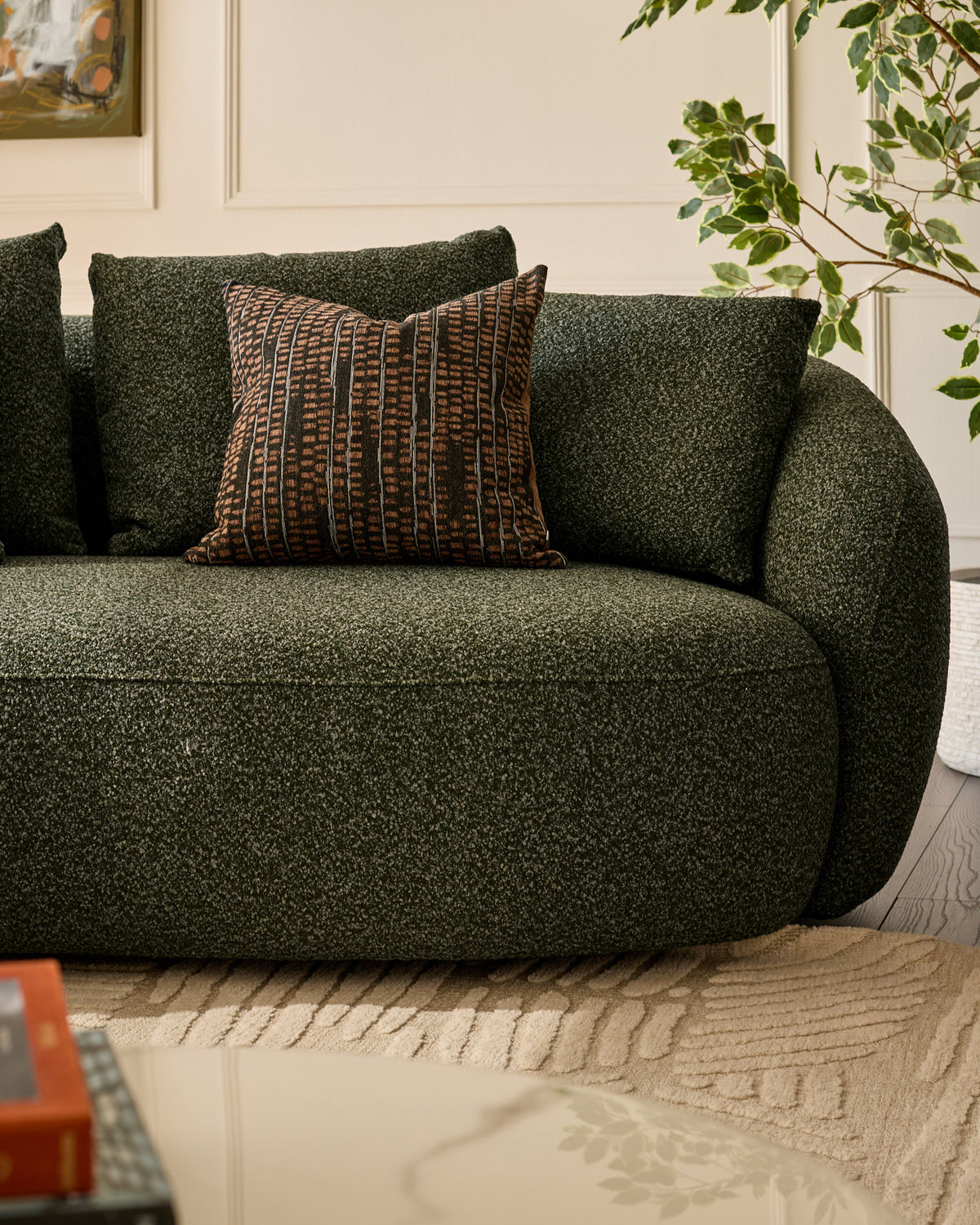 Dark green upholstered left-hand corner chaise sofa with curved arms and patterned cushion, styled in a bright modern room.