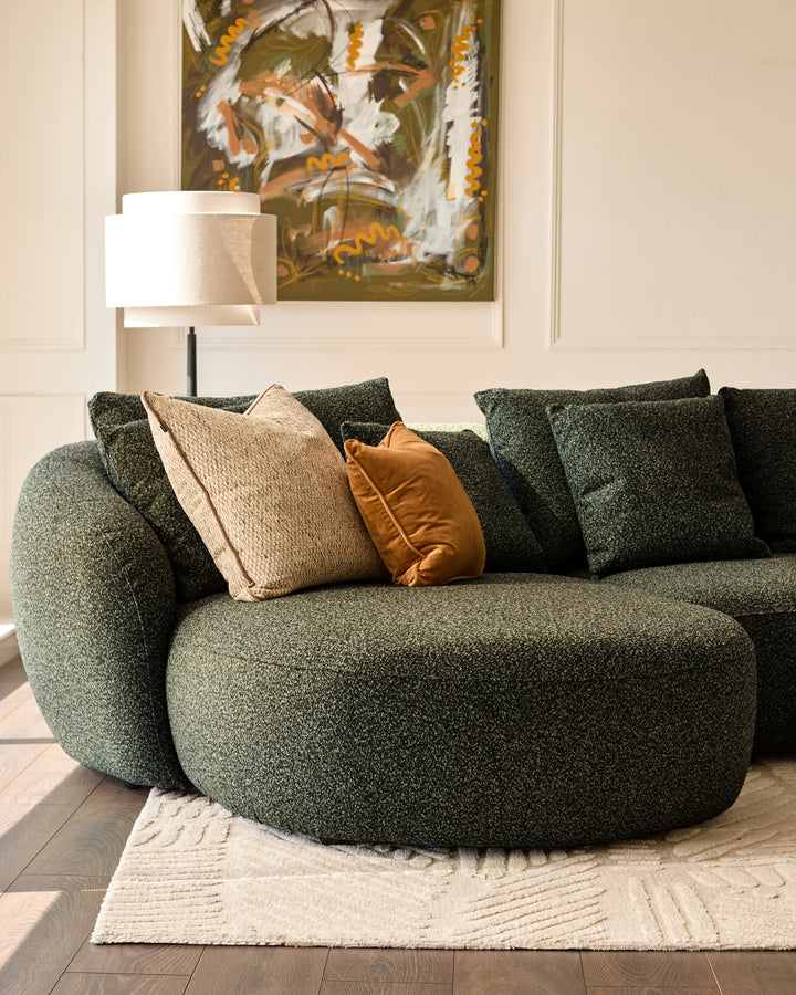 Eris left-hand corner chaise sofa in dark green fabric, styled with patterned pillows and a cream rug in a bright interior.