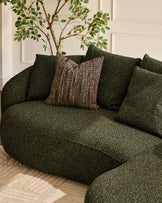 Eris right-hand corner chaise sofa in dark green fabric with patterned throw pillow and potted plant detail.