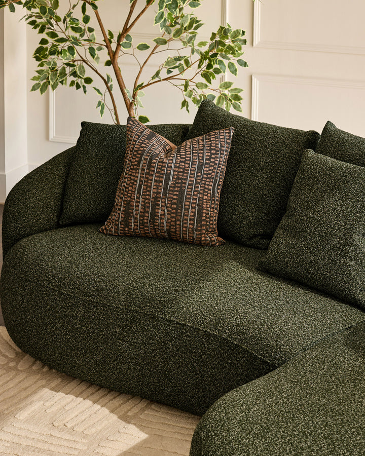 Eris right-hand corner chaise sofa in dark green fabric with patterned throw pillow and potted plant detail.