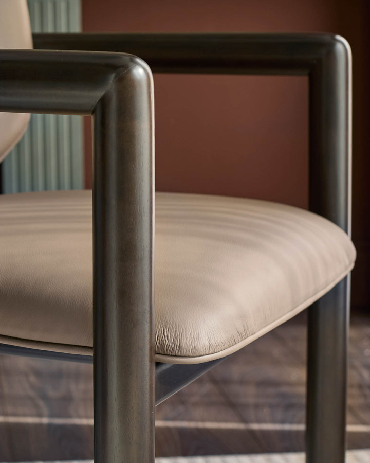 Esme dining chair in mocha leather, close-up of curved metal frame and seat cushion detail.