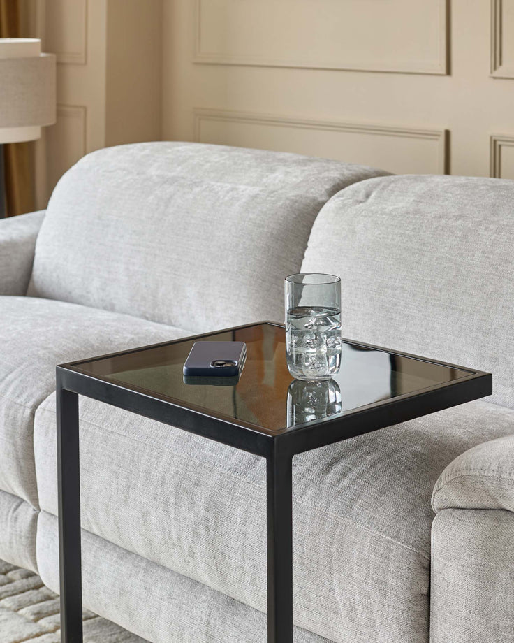 Ezra tray table with smoked glass top and black metal frame, styled next to a cream upholstered sofa.