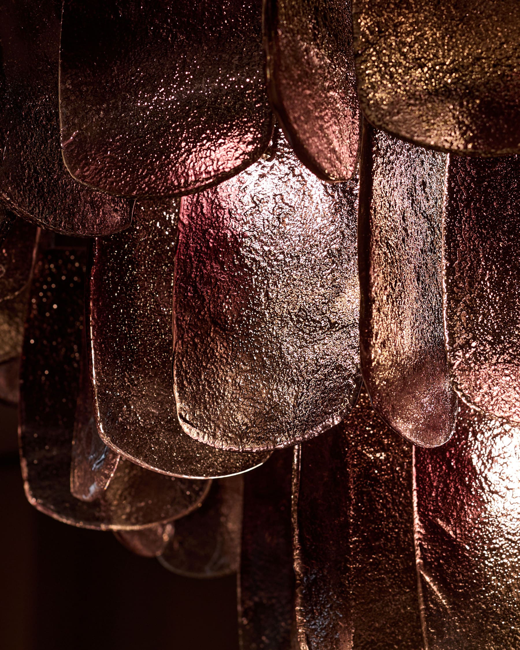 Estelle chandelier close-up showing smoked glass with golden-bronze ombre finish and textured surface detail.