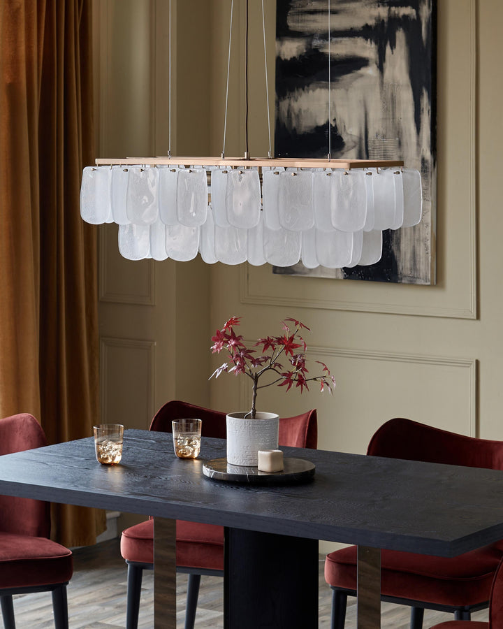 A dining room featuring a dark wood table, plush velvet chairs, statement chandelier and decorative pieces.