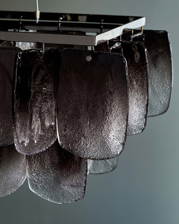 A stylish chandelier featuring textured, translucent panels suspended from a chrome frame, creating a modern focal point.