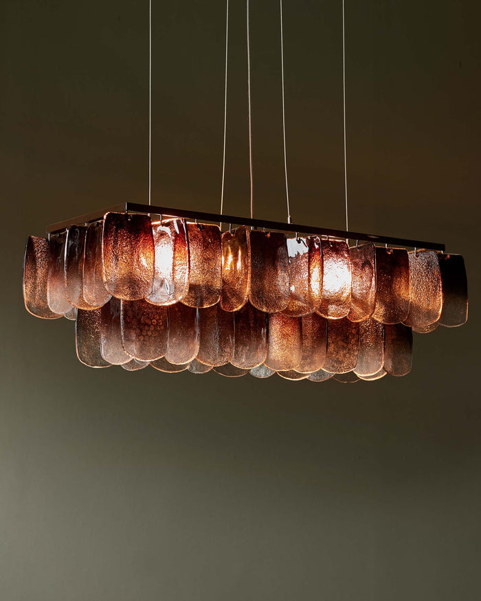 Rectangular chandelier with textured glass panels, suspended from a metal frame. It creates a warm lighting effect.