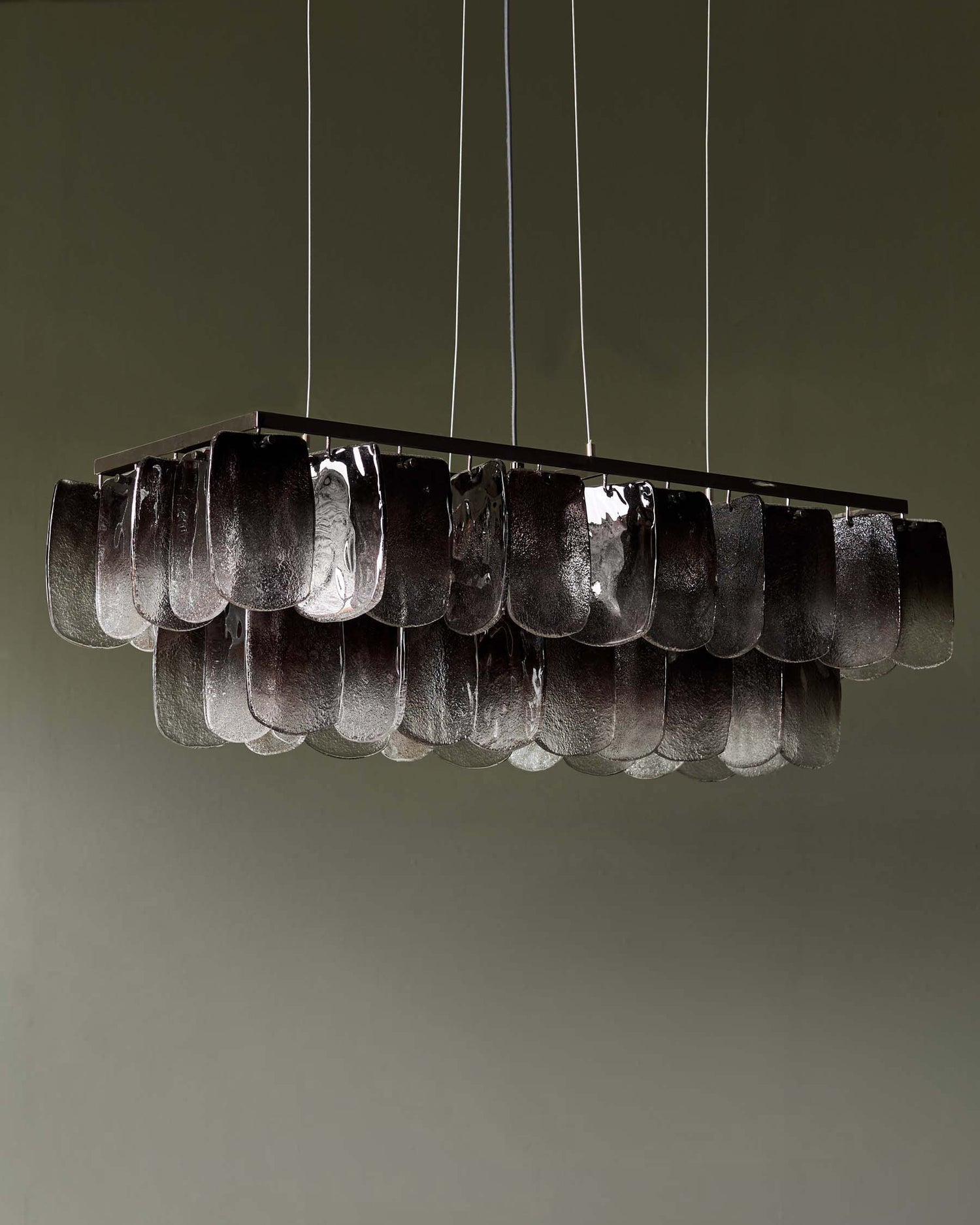 A rectangular chandelier with textural glass elements, suspended by slim cables, adds a touch of modern elegance.
