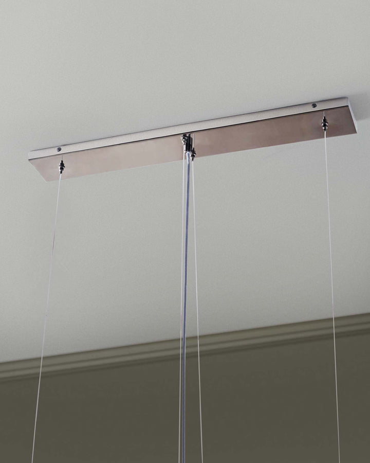 Close-up of a modern pendant light fixture with a sleek, rectangular, brushed metal canopy mounted to a light grey ceiling.