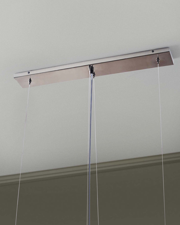 Close-up of a modern pendant light fixture with a sleek, rectangular, brushed metal canopy mounted to a light grey ceiling.