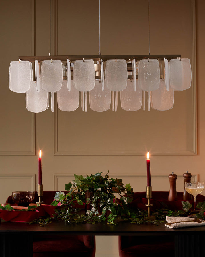 Elegant dining area with a modern chandelier, candlelit table, and plush velvet chairs for a luxurious atmosphere.