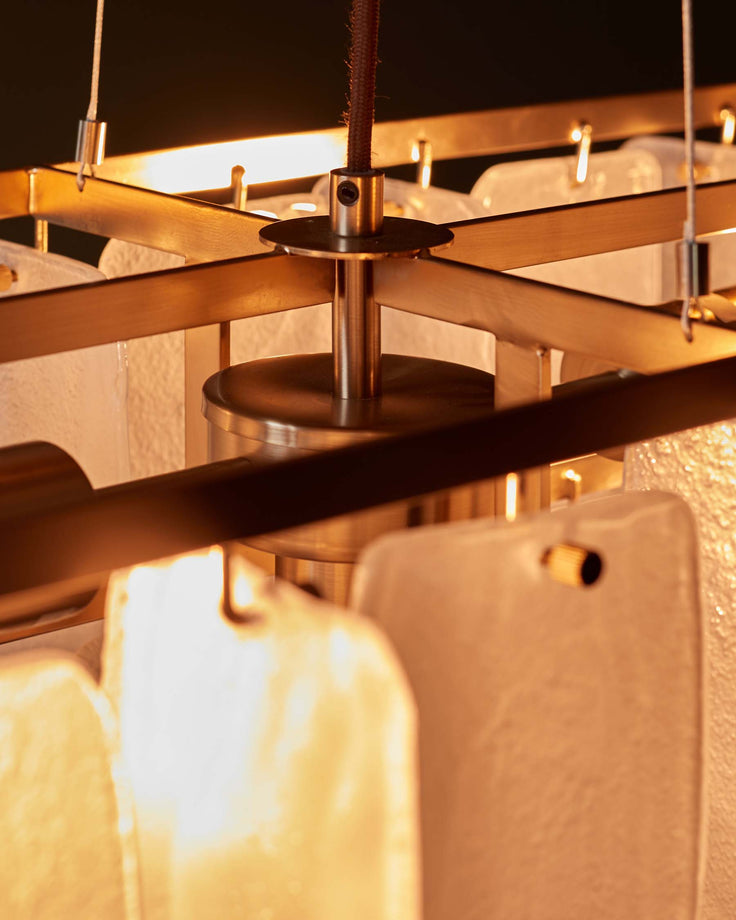 Close-up of a modern chandelier with a gold frame and decorative translucent white panels. Features a central metal fitting.