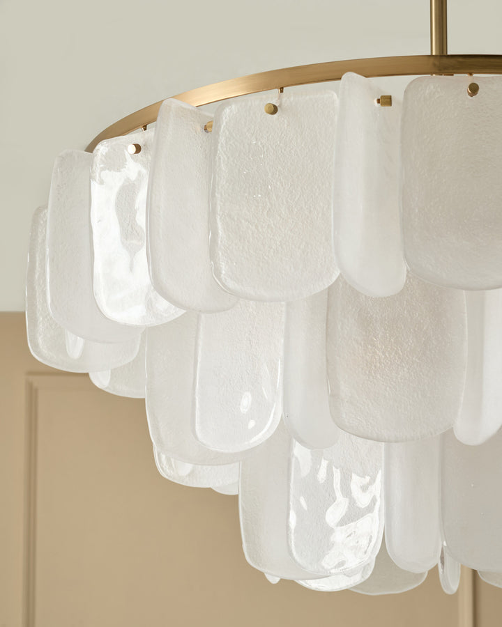 Estelle chandelier with curved brass rod and white textured glass panels hung from brass rings against neutral wall.