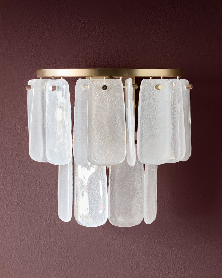 Estelle wall light with brass fixture and cascading white textured glass panels against burgundy wall.