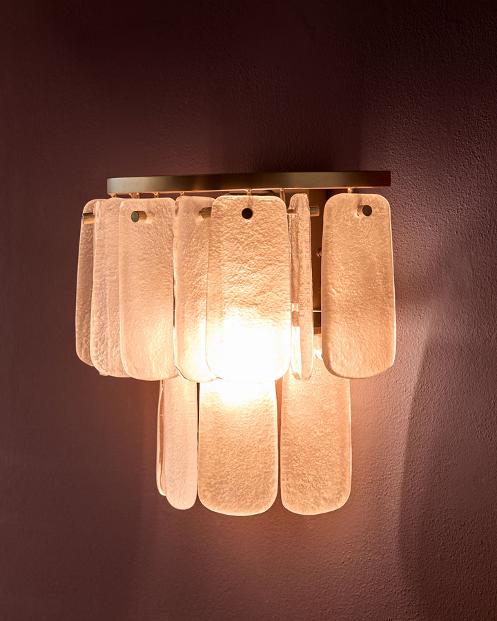 Estelle wall light with frosted glass panels in white, mounted on wall, glowing warm light from within.