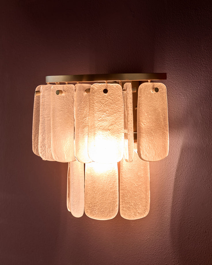 Estelle wall light with frosted glass panels in white, mounted on wall, glowing warm light from within.