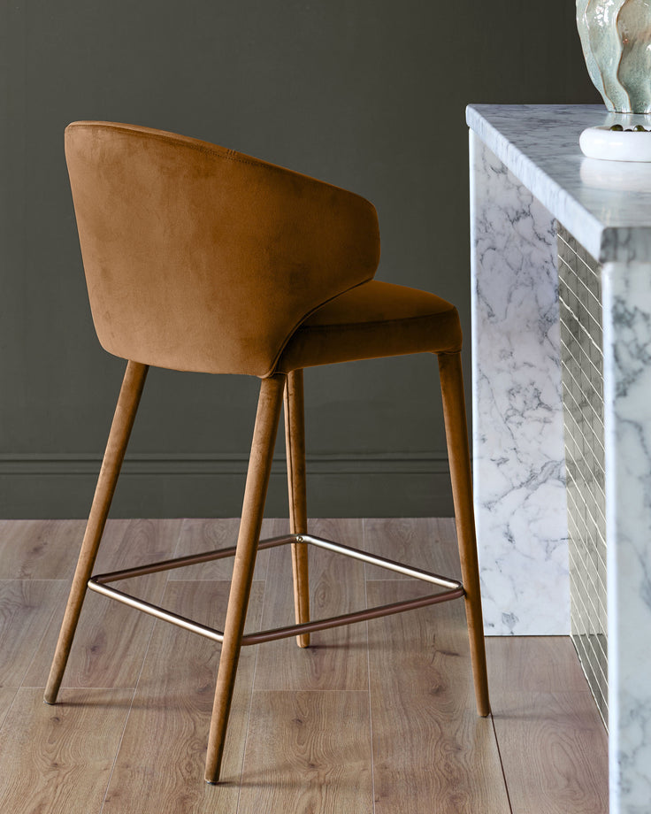 Caramel fabric bar stool with wooden legs and metal footrest, shown from back angle in modern interior setting.