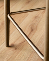 Close-up of brushed metal footrest and leg detail on caramel fabric bar stool against wooden floor.