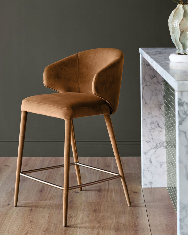 Caramel fabric bar stool with curved back, wooden legs, and metal footrest, styled in modern interior setting.