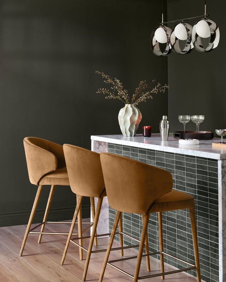 Caramel fabric bar stool with wooden legs, shown in modern kitchen setting at marble counter.