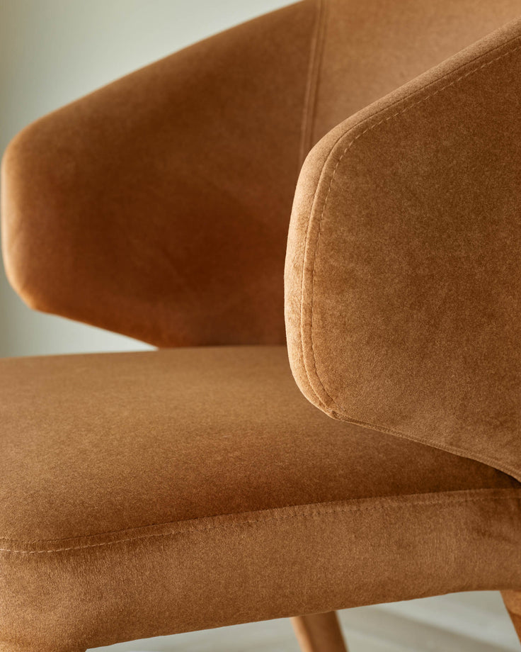 Close-up of a brown chair with armrests. The chair has a soft, velvety texture and a minimalist design.