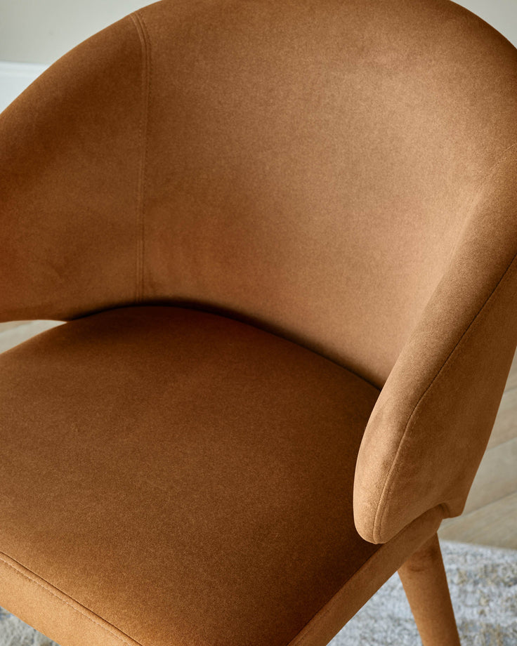 Close-up of a stylish, tan-coloured armchair. The plush seat and armrests offer comfort and sophistication.