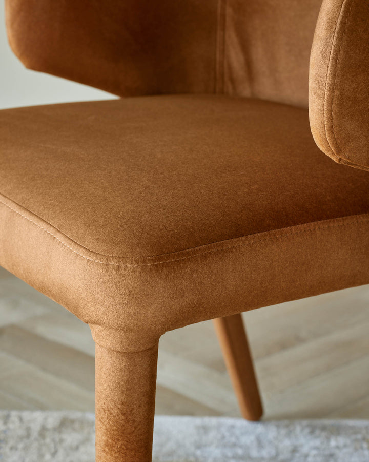 Close up of a brown upholstered chair with a seam line on the seat and a wooden leg.