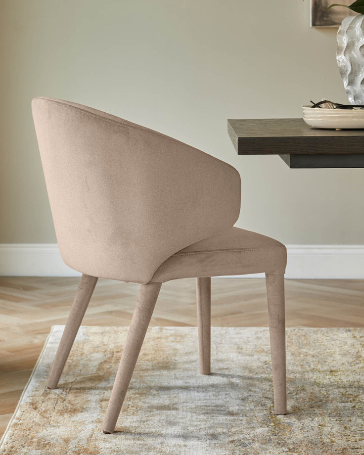 Ethan dining chair in champagne velvet, shown from rear angle with curved backrest and tapered legs on a neutral area rug.