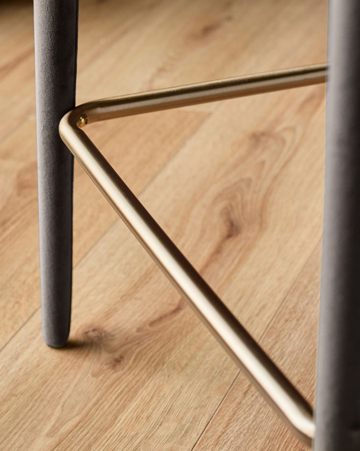 Ethan bar stool detail: brass footrest and Grey upholstered leg on wooden floor.