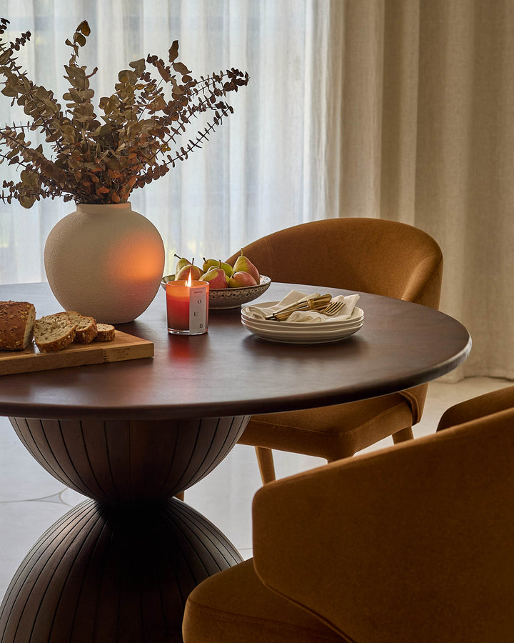 Malin 4-seater dark mango wood dining table with round top and sculptural pedestal base, styled with chairs and tableware.