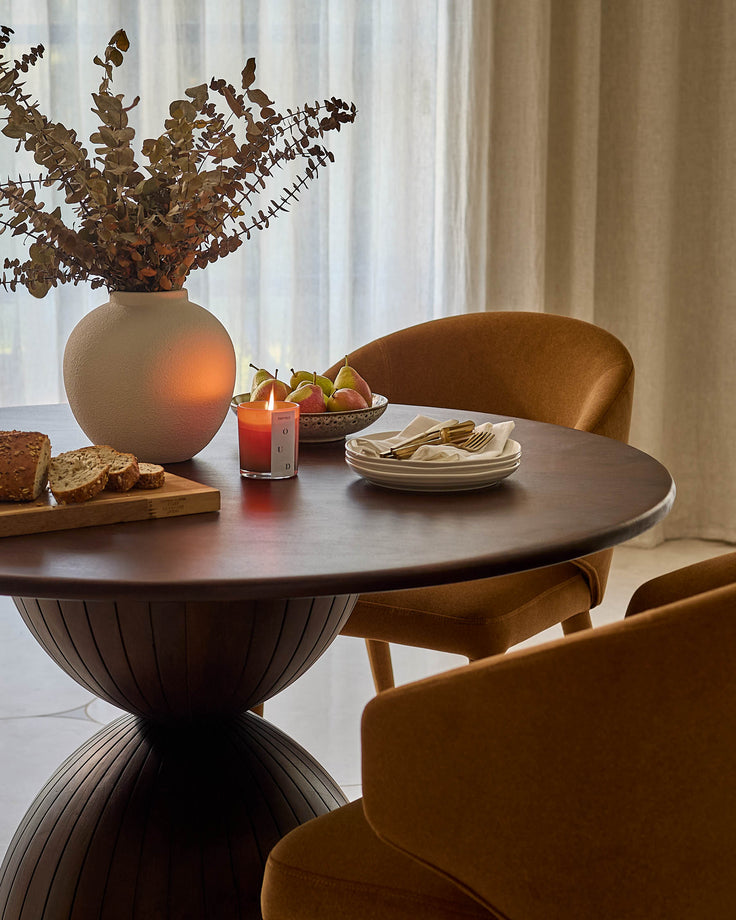 Malin 4-seater dark mango wood dining table with round top and sculptural pedestal base, styled with chairs and tableware.