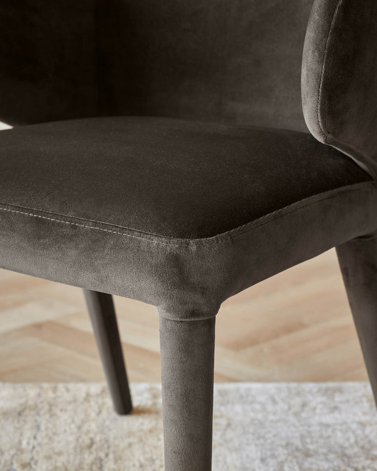 Close-up of a stylish, brown velvet chair with a curved armrest and plush seat, showcasing its elegant design and comfort.