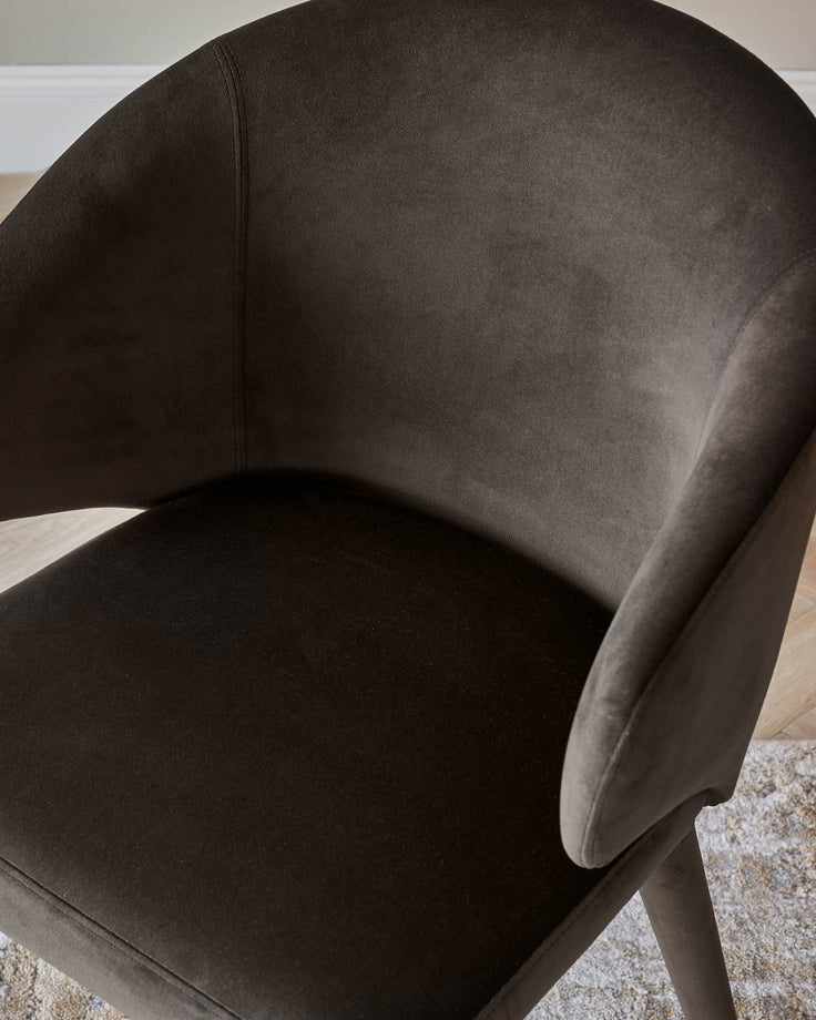 Close-up of a stylish, brown velvet armchair, showcasing its curved design and plush upholstery.