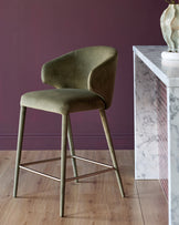 Ethan bar stool in olive green velvet with curved backrest, wooden legs, and metal footrest against purple wall.