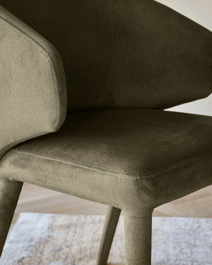 Close up of a stylish, olive green chair with upholstered seat, arms and legs.