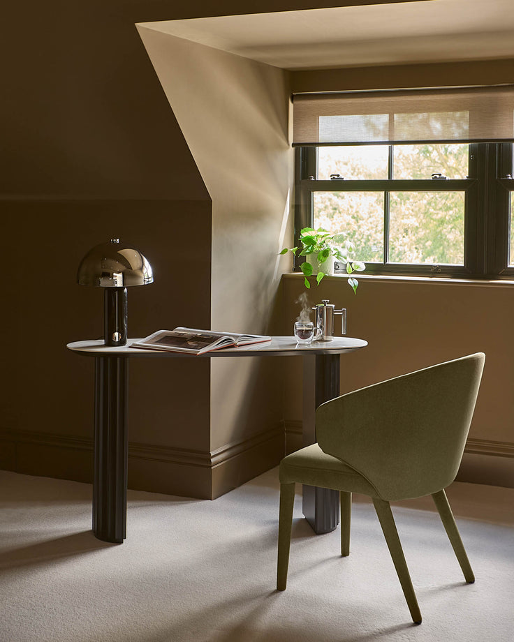 Hanne console table in white ceramic with dark metal base, styled in a modern workspace with a green chair and brass lamp.