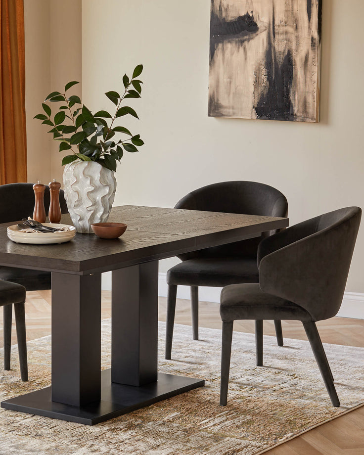 A dark wood dining table with matching upholstered chairs, set on a patterned rug. An abstract painting hangs on the wall.