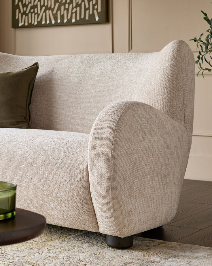 Evelyn 2-seater sofa in natural fabric, curved armrest detail, cylindrical legs, displayed in modern living room setting.