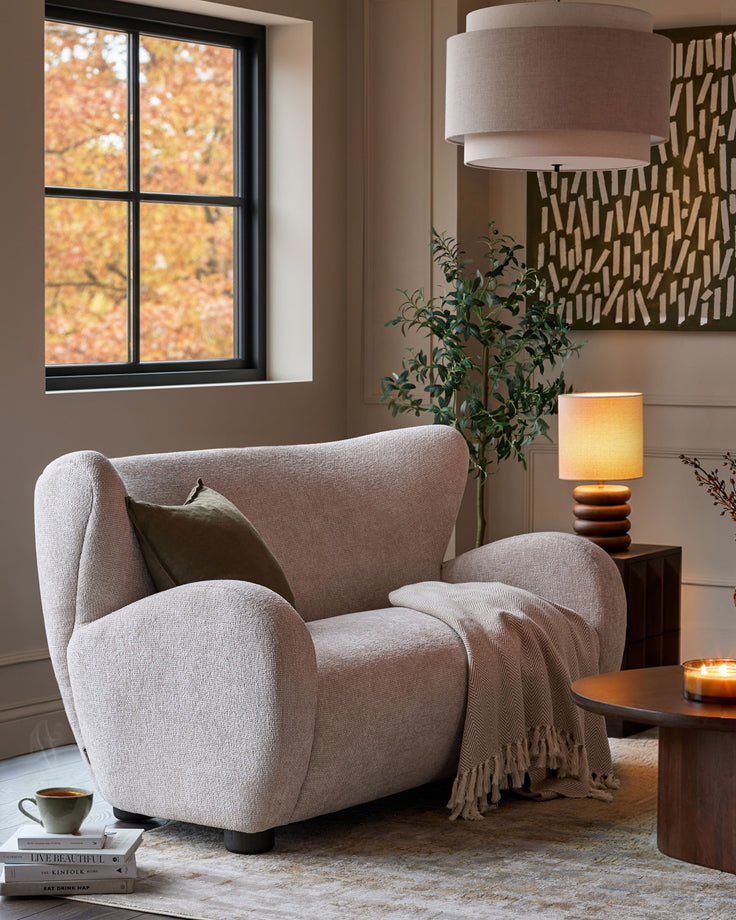Cream fabric 2-seater sofa with curved arms and rounded back, displayed in a cozy living room setting.