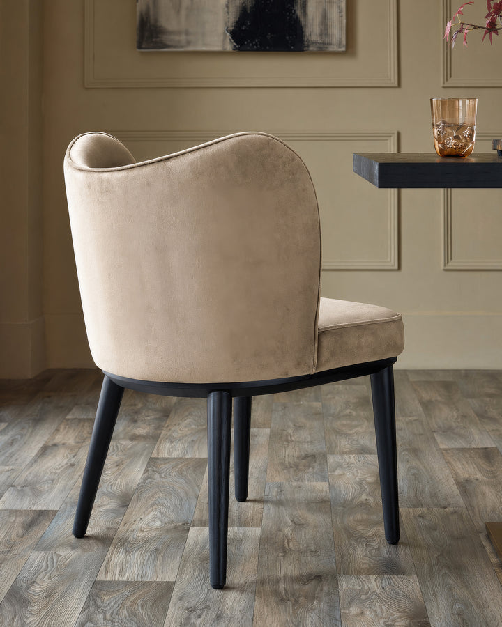 Evelyn dining chair in champagne velvet with black wooden legs, shown from rear three-quarter view in a styled room setting.